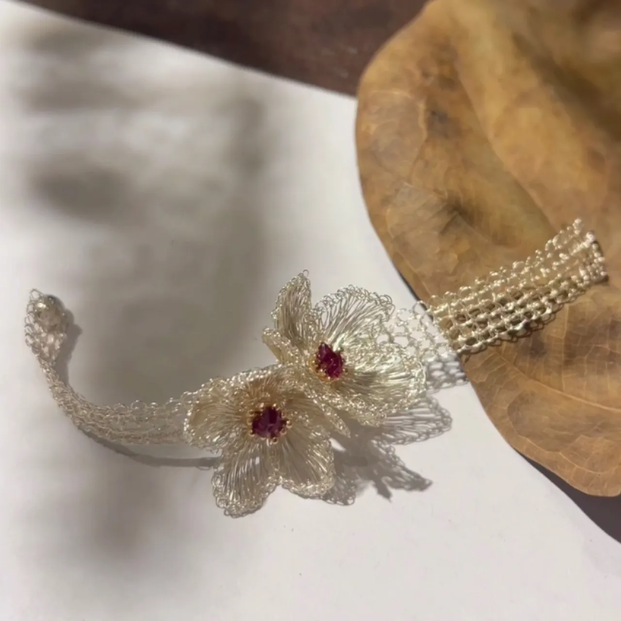Silver-tone handwoven wire bracelet with two sculptural flowers and magenta faceted center accents