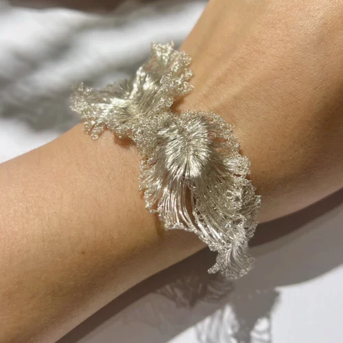 Close-up of a sculptural silver-tone wire flower cuff bracelet worn on the wrist