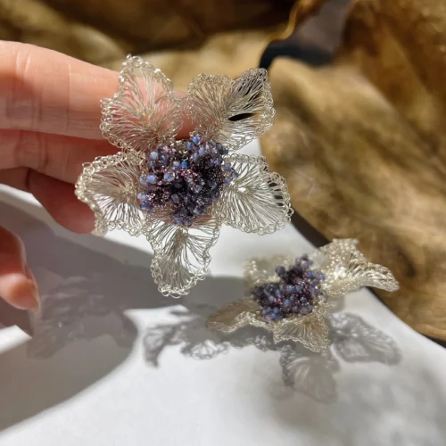 Handheld close-up of a silver-tone wire flower earring with woven petals and a purple-blue beaded center