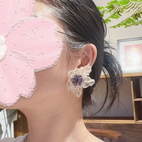 Model wearing a silver-tone wire flower statement earring with a clustered purple and blue beaded center
