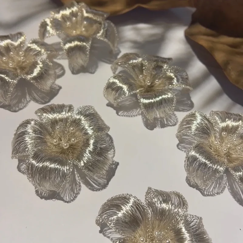Small batch of handwoven metallic flower brooches arranged on a white surface.