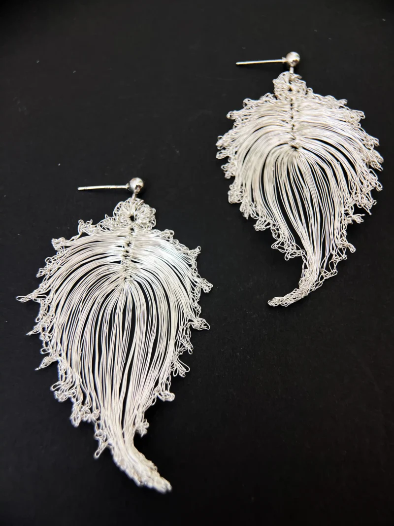 Pair of handwoven bodhi leaf drop earrings on a dark background